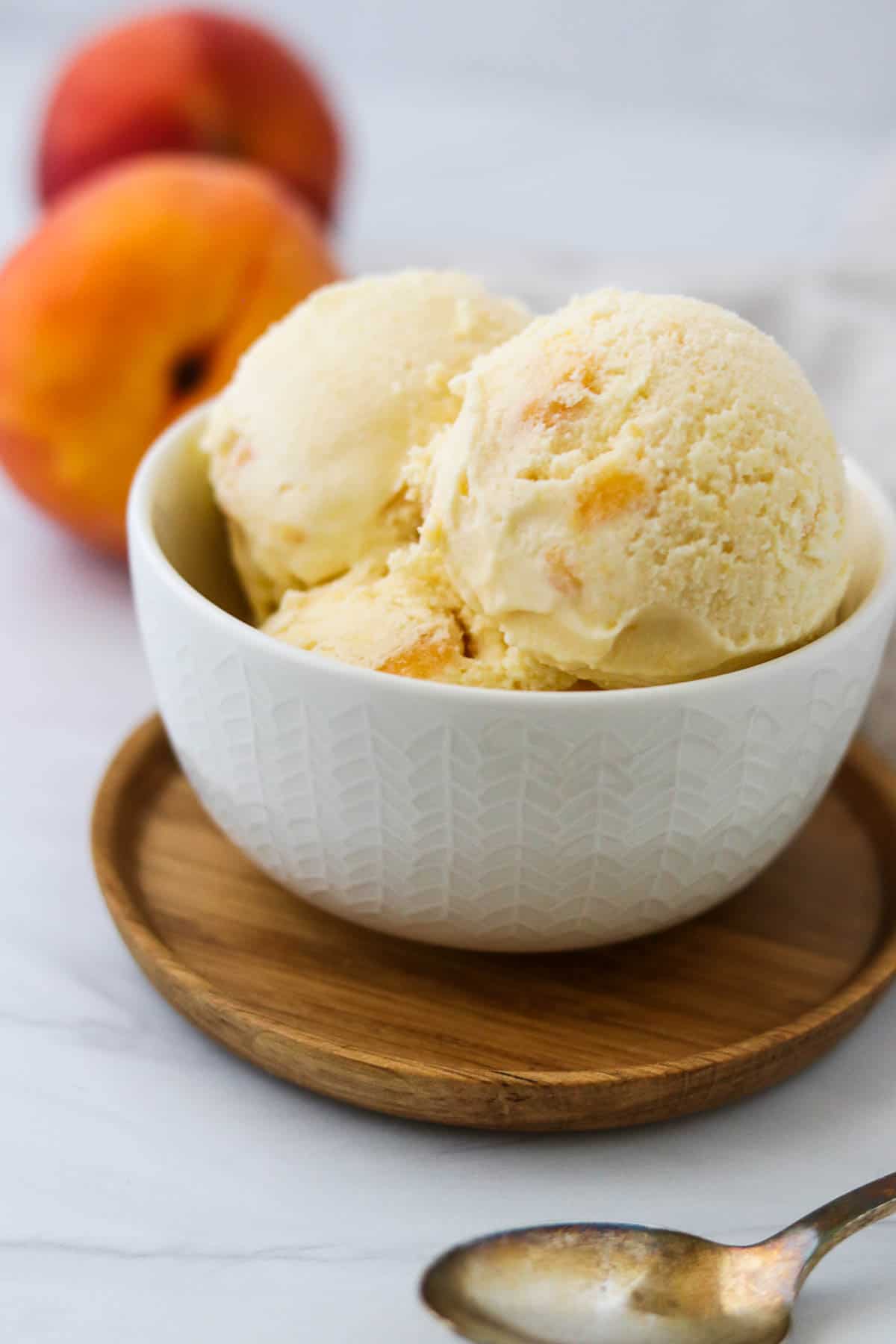 Peaches and Cream Ice Cream in a bowl next to a spoon and peaches.