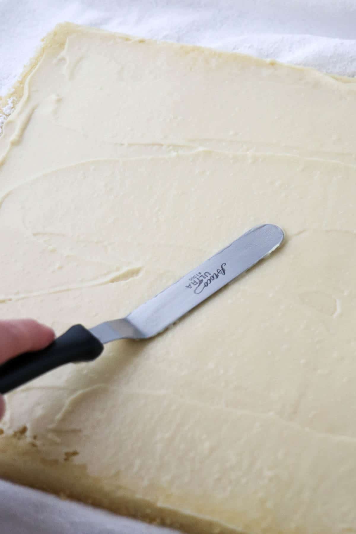 Person spreading pastry cream over the surface of a vanilla cake.