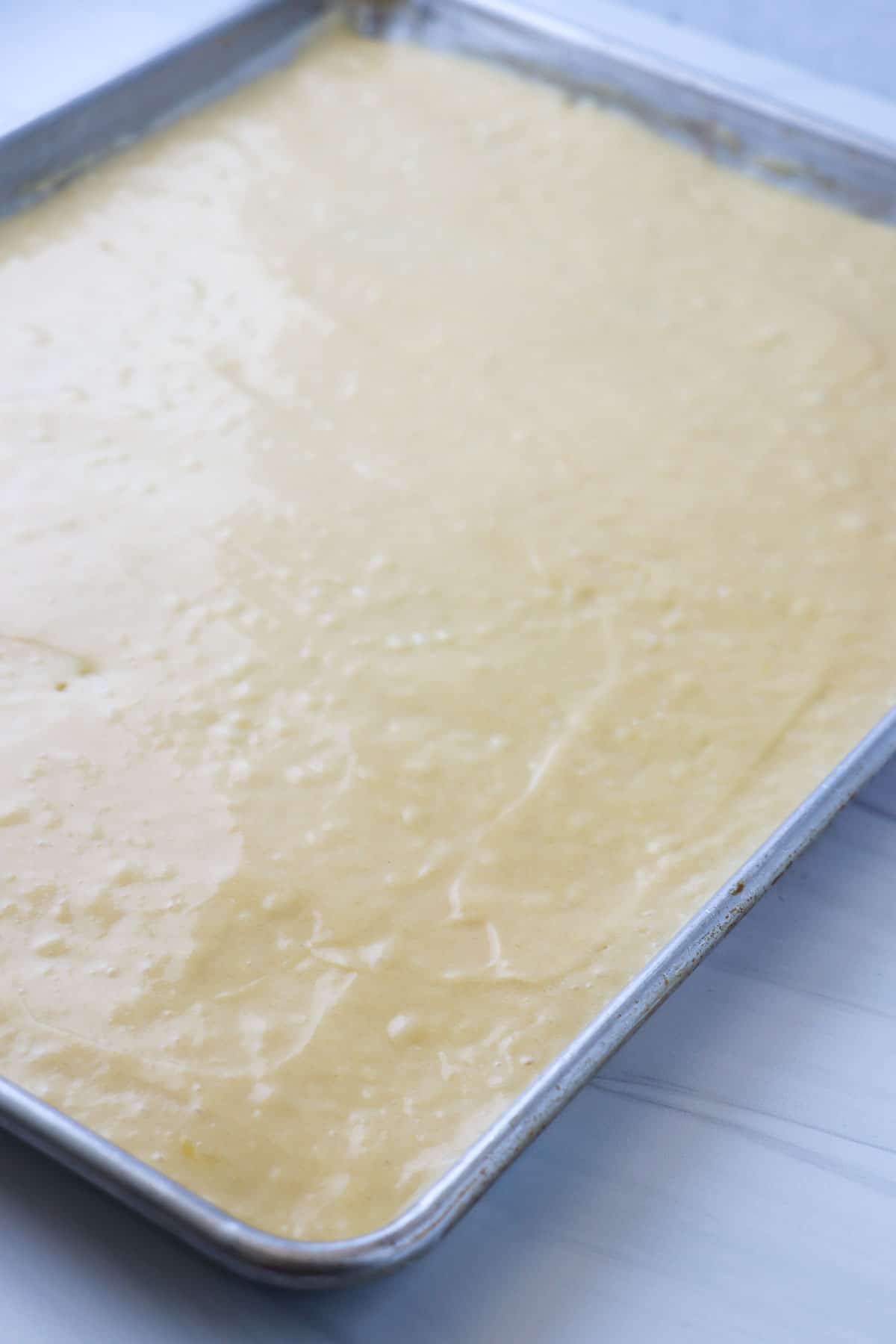Vanilla cake batter spread out in a sheet pan.