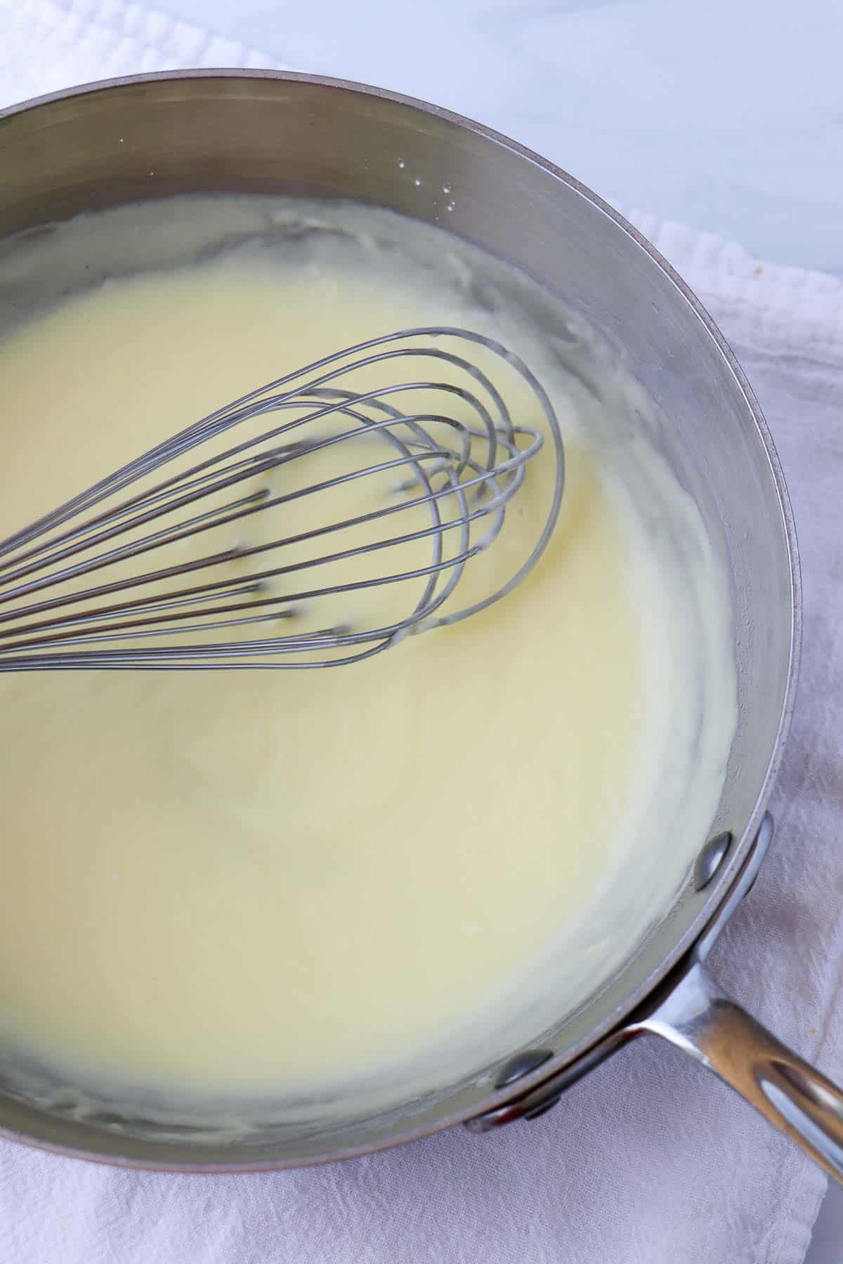 Pastry cream in a saucepan with a whisk.