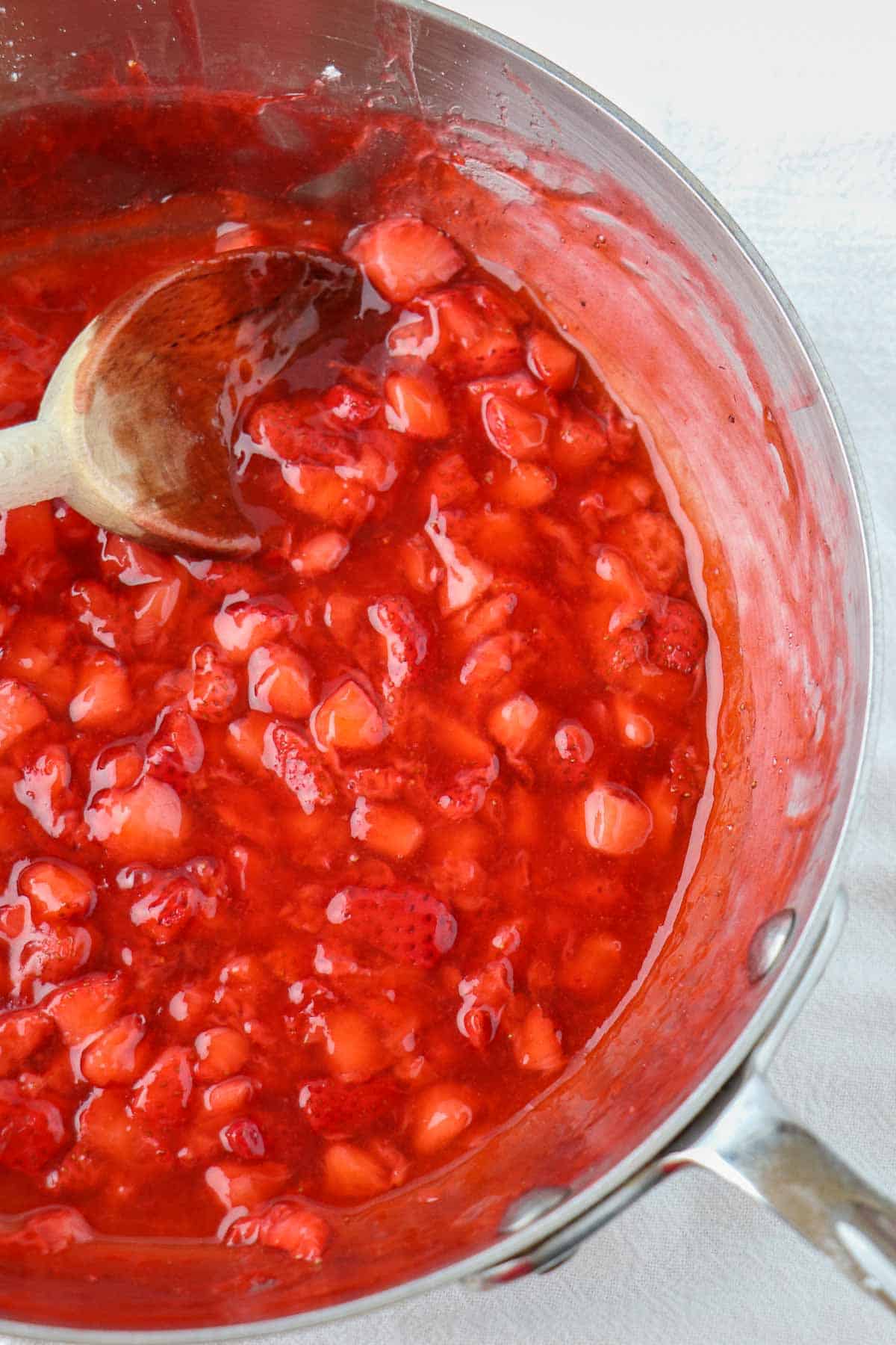 Strawberry filling in a saucepan with a wooden spoon.