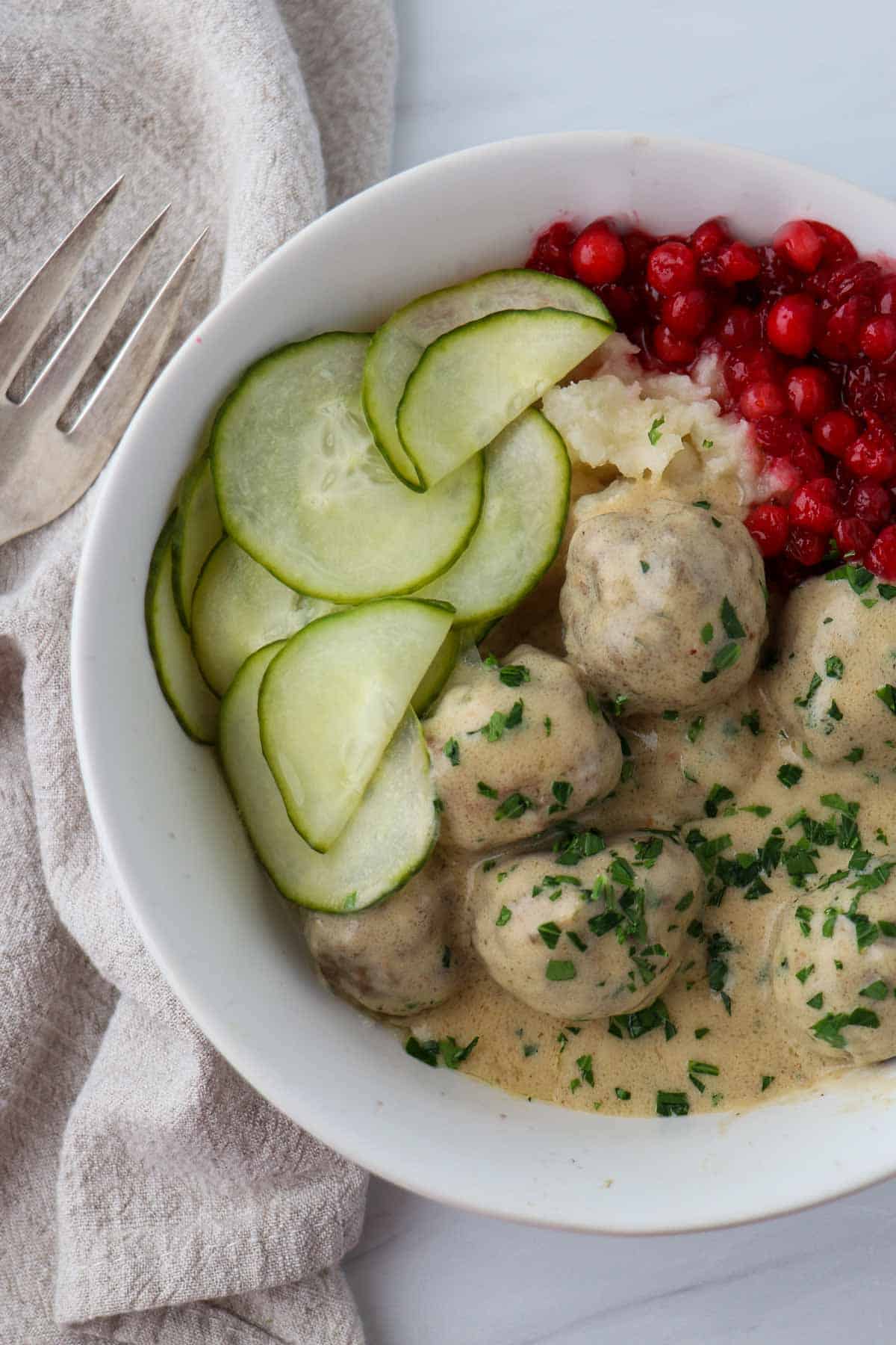 Overhead shot of Swedish Meatballs with Gravy and pickles and lingonberries.