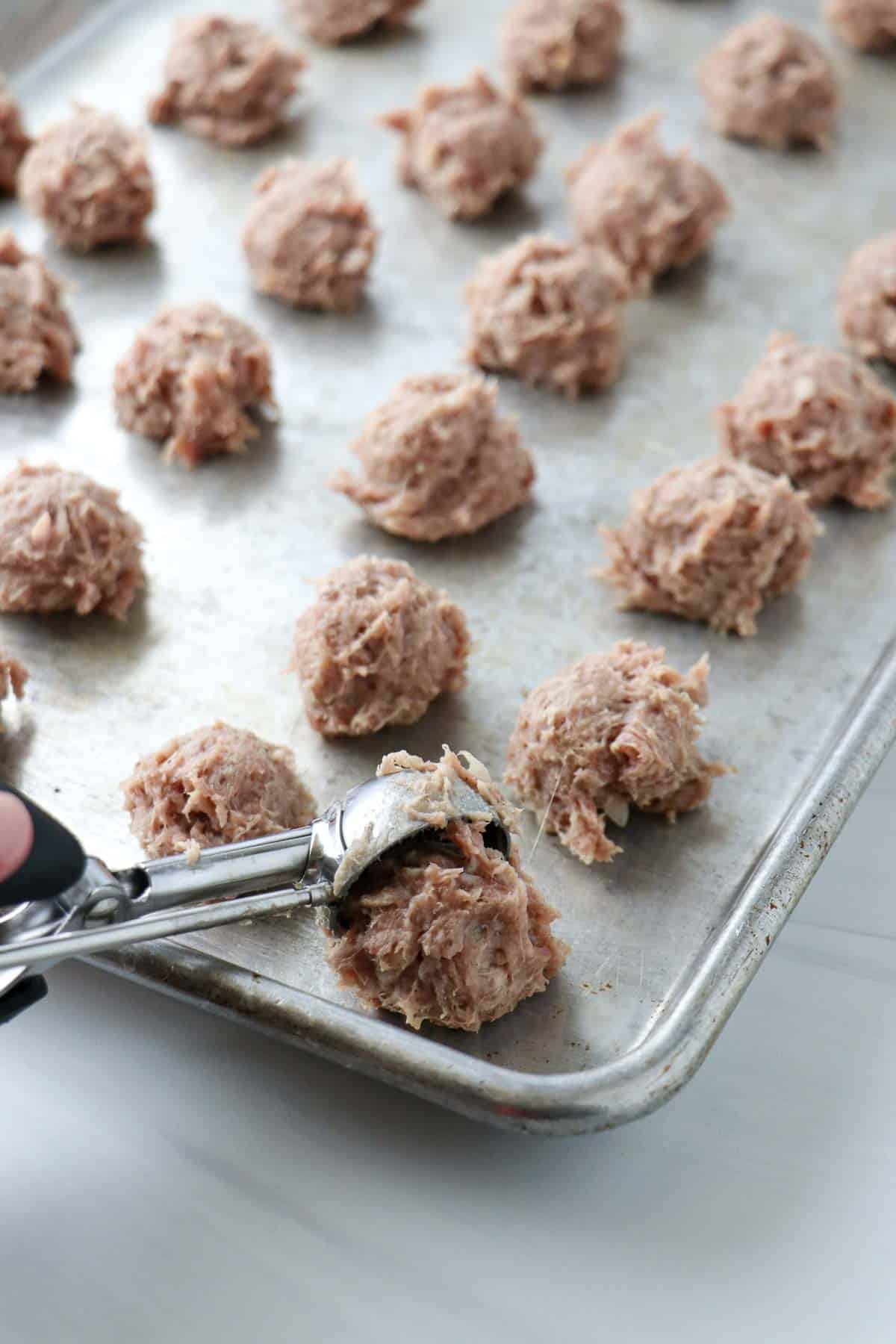 Person dropping tablespoons of meatball mix onto a baking sheet.
