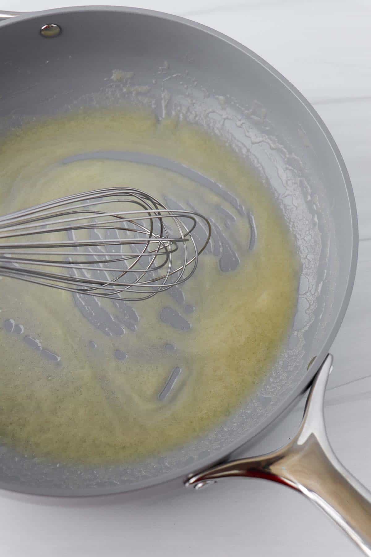 Melted butter in a gray skillet with a whisk.