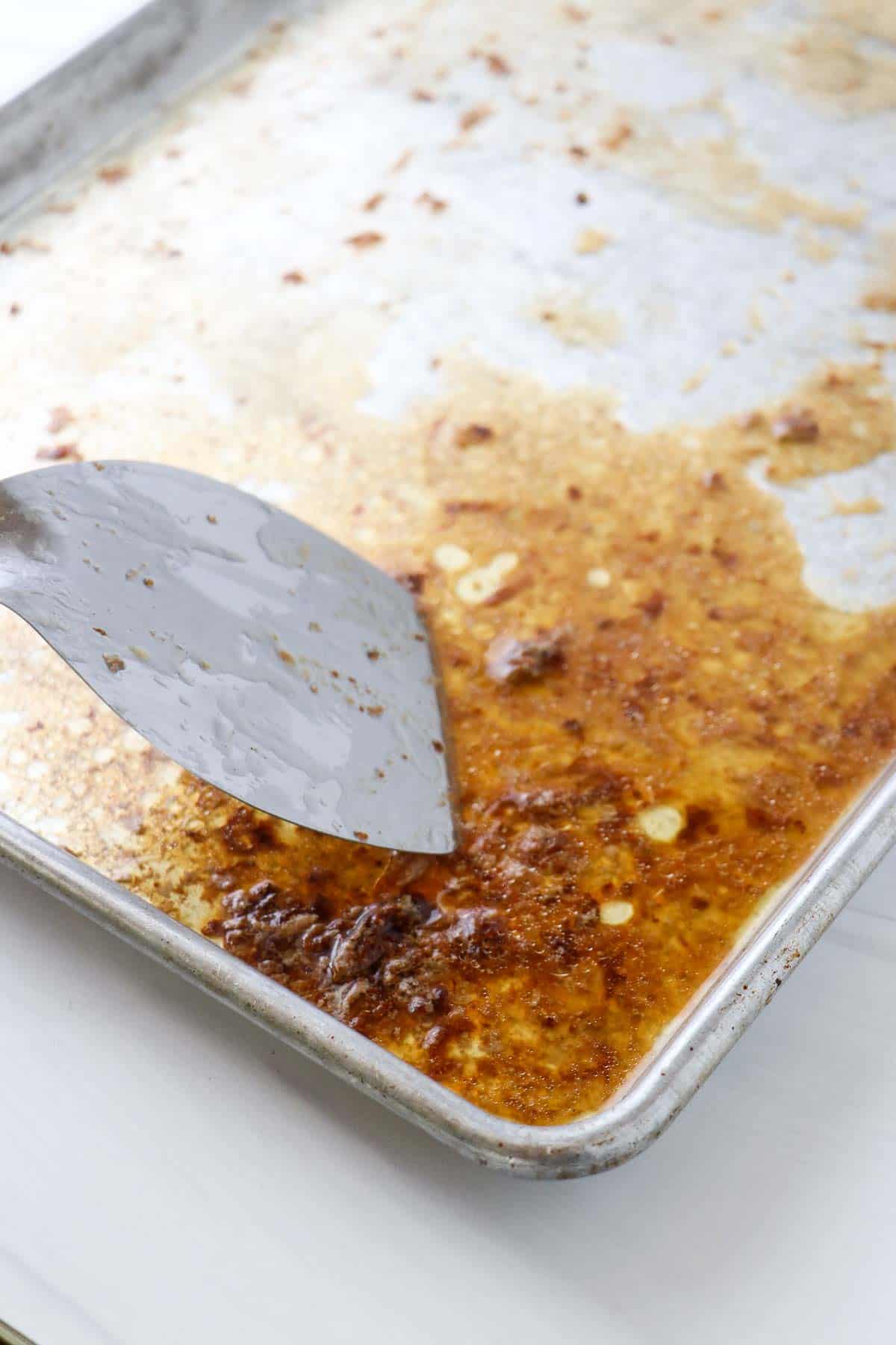 Baking sheet with brown bits and a metal spatula.