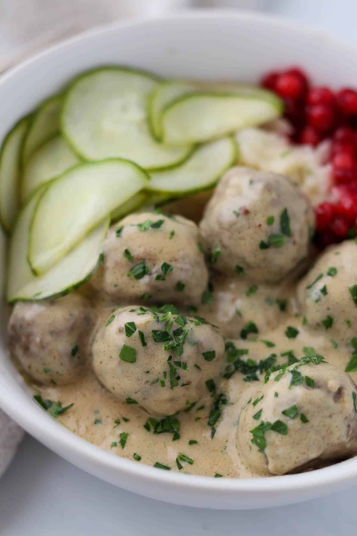 Close up of Swedish Meatballs with Gravy and pickles and lingonberries.