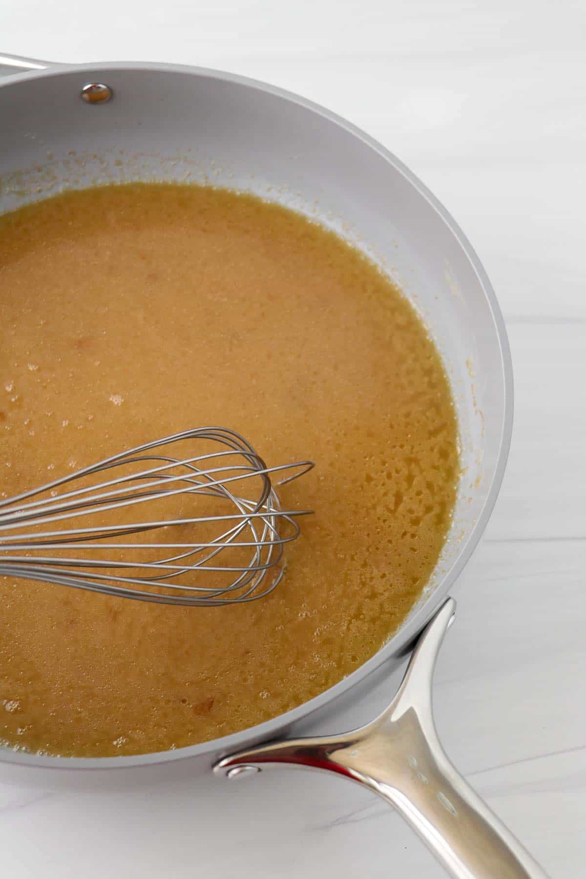 Broth in a gray pan with a whisk.