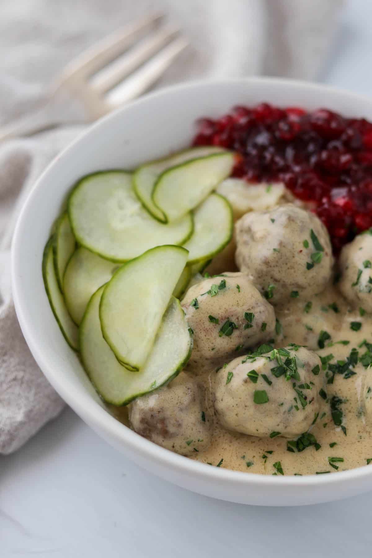 Side view of Swedish Meatballs with Gravy and pickled cucumbers and lingonberry jam.