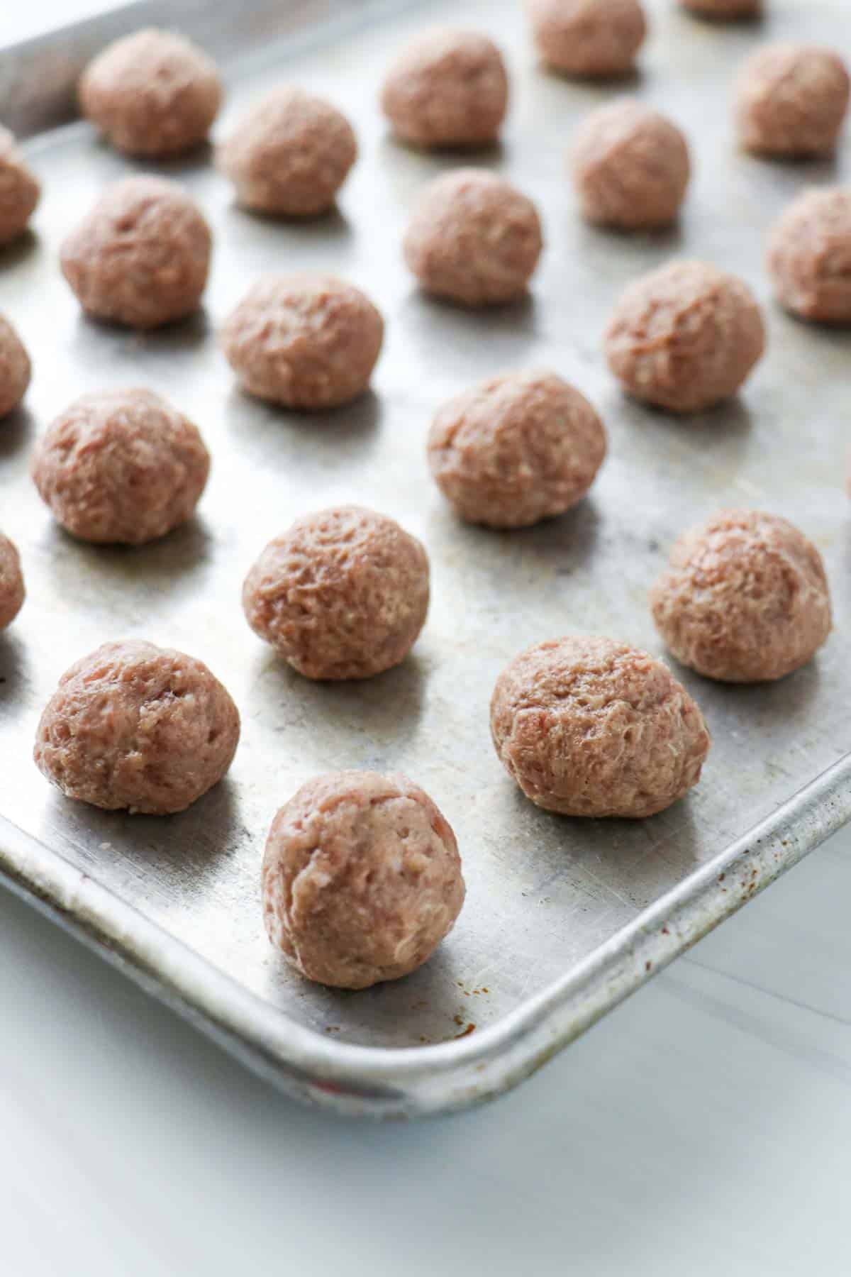 Uncooked, rolled Swedish Meatballs on a baking sheet.