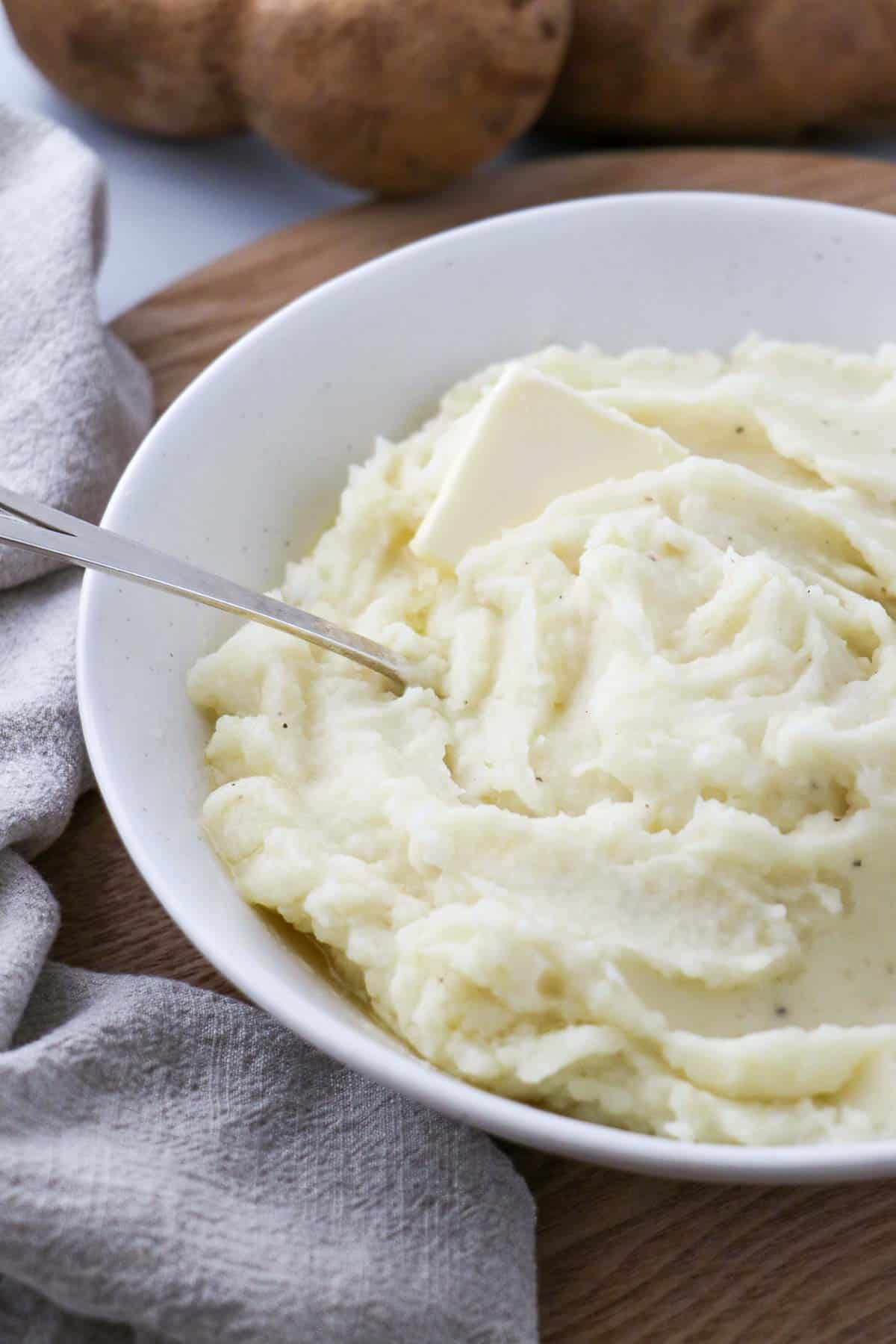 Side view of mashed potatoes in a bowl with butter and a spoon.