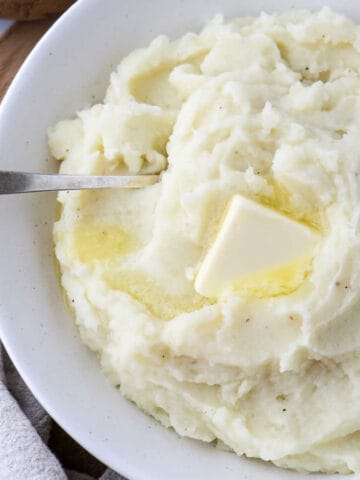 Overhead shot of mashed potatoes in a white bowl topped with butter with a spoon.