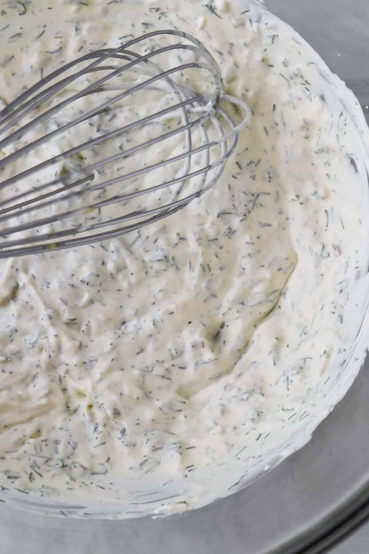 Creamy dill dressing in a glass bowl with a whisk.