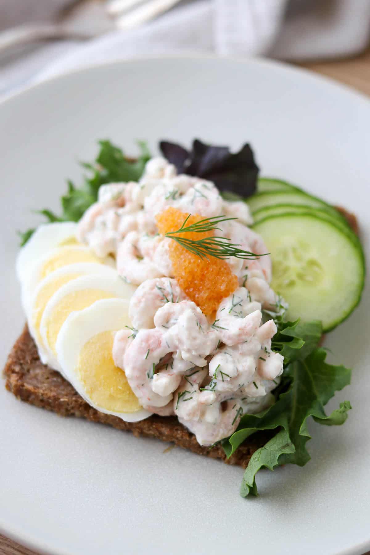 Skagenröra on rye bread with sliced hard boiled egg and sliced cucumber and topped with caviar.