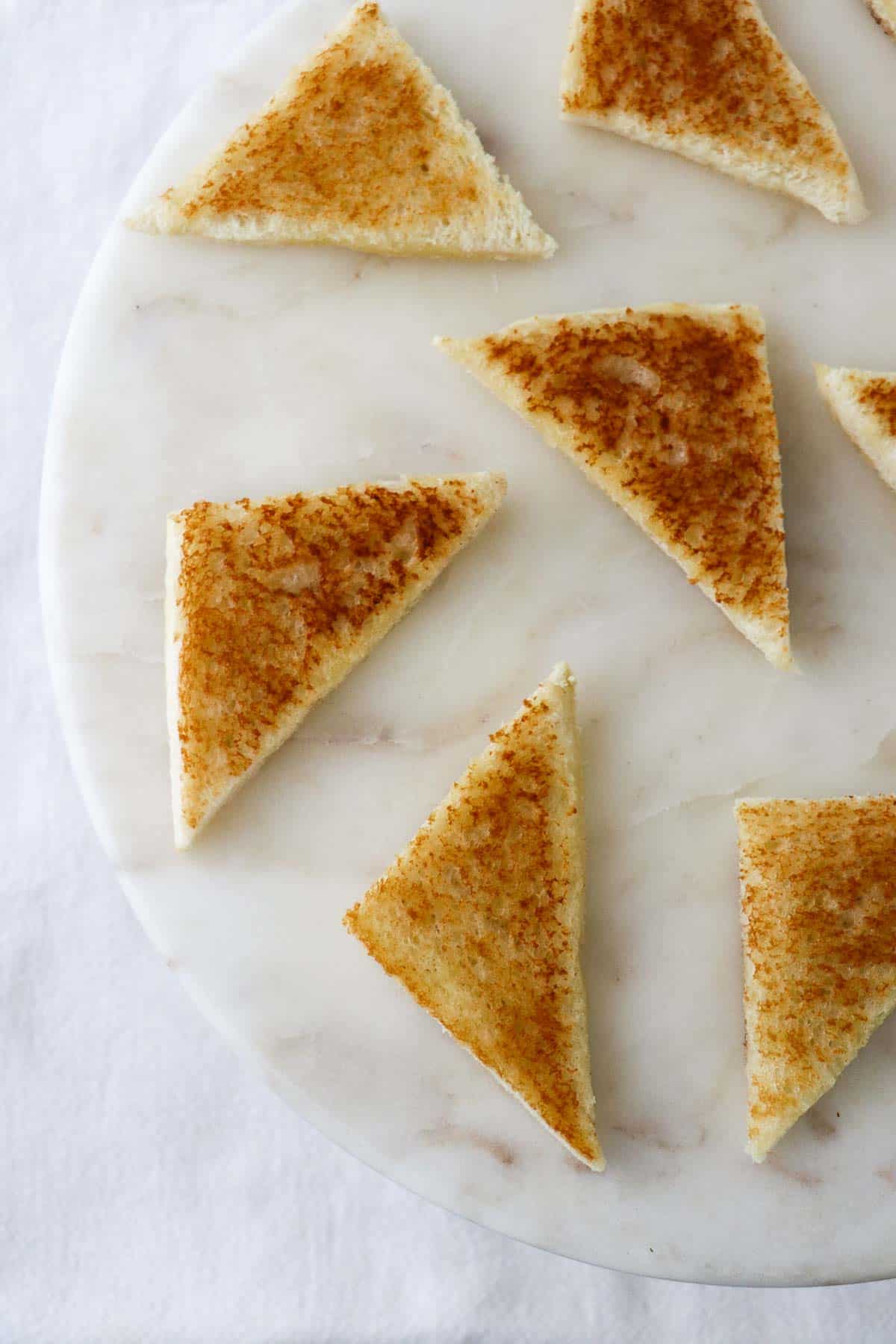 Crispy white bread toast triangles on a marble serving platter.