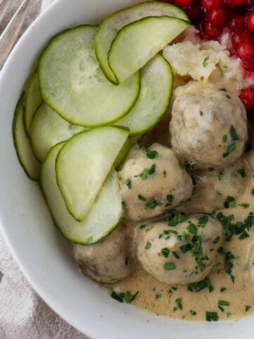 Overhead shot of Swedish Meatballs in a bowl with cucumbers and lingonberries.