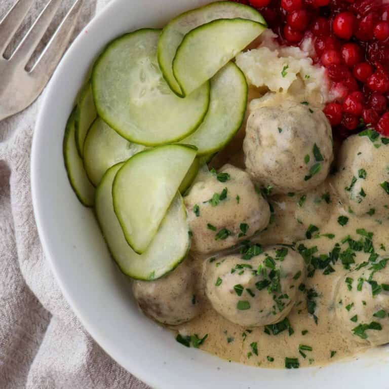 Overhead shot of Swedish Meatballs in a bowl with cucumbers and lingonberries.