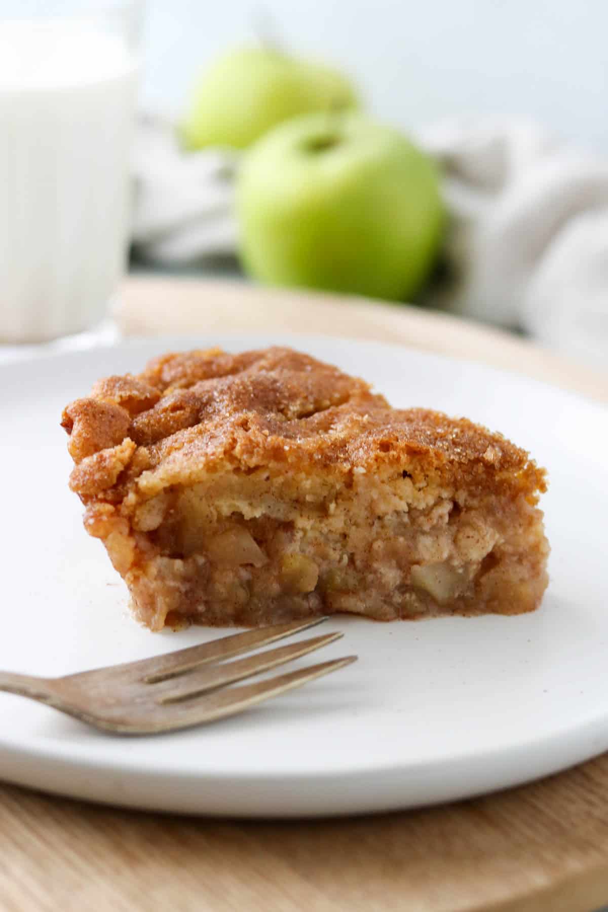 Slice of Swedish Apple Pie on a plate next to a fork and a glass of milk.