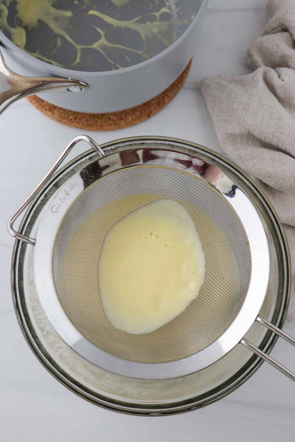 Vanilla sauce in a strainer over a glass bowl.