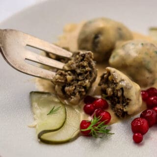 Vegetarian Swedish meatballs on a plate with a fork lingonberries and a pickle.