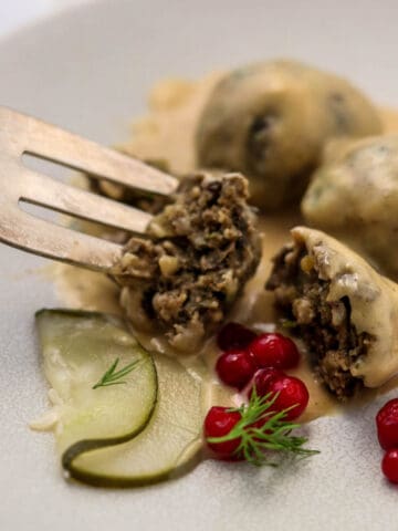 Vegetarian Swedish meatballs on a plate with a fork lingonberries and a pickle.