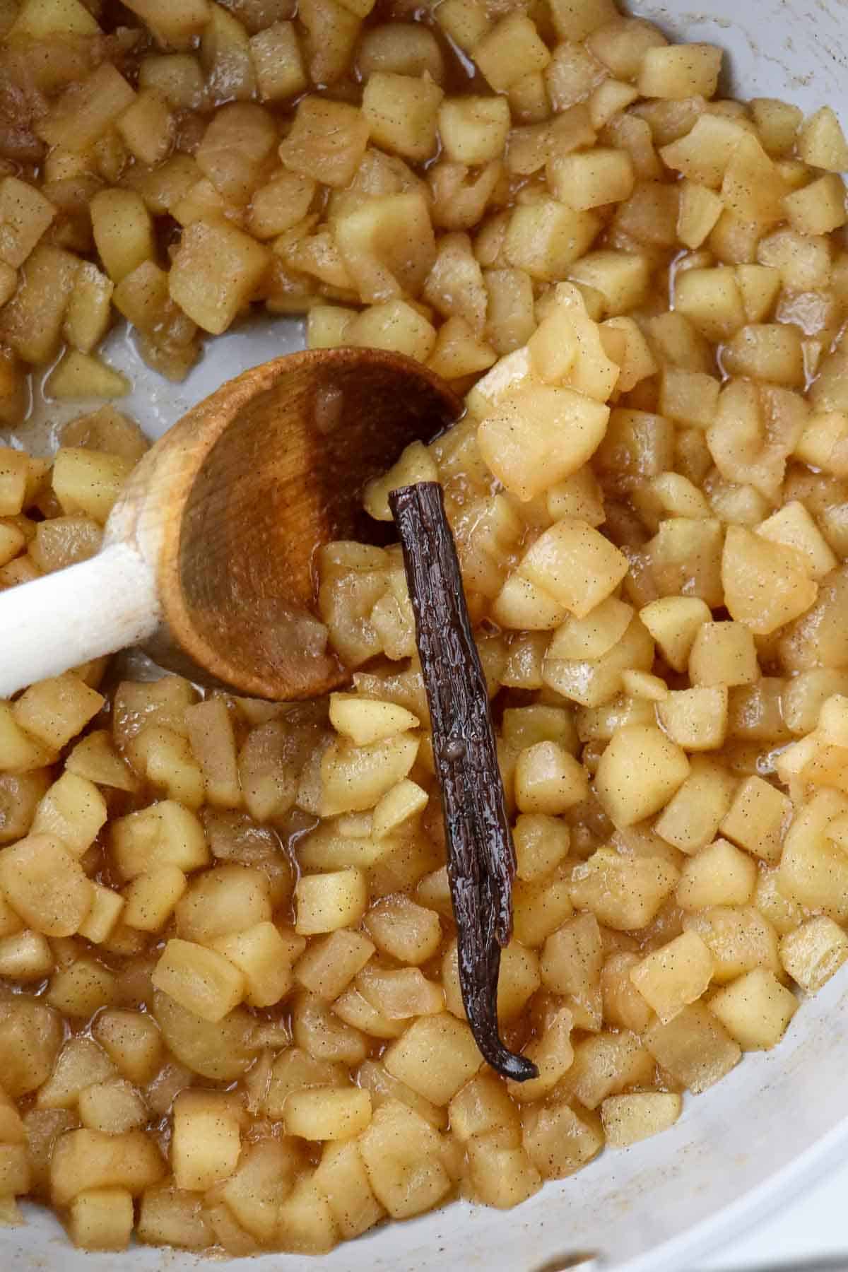 Apple compote and a vanilla bean in a saucepan with a wooden spoon.