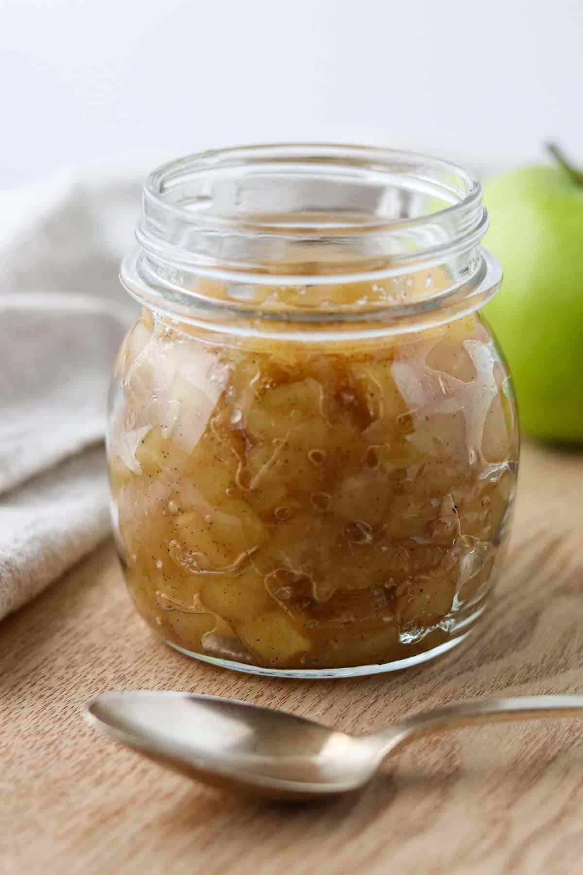 Apple compote in a jar next to a spoon and a green apple.