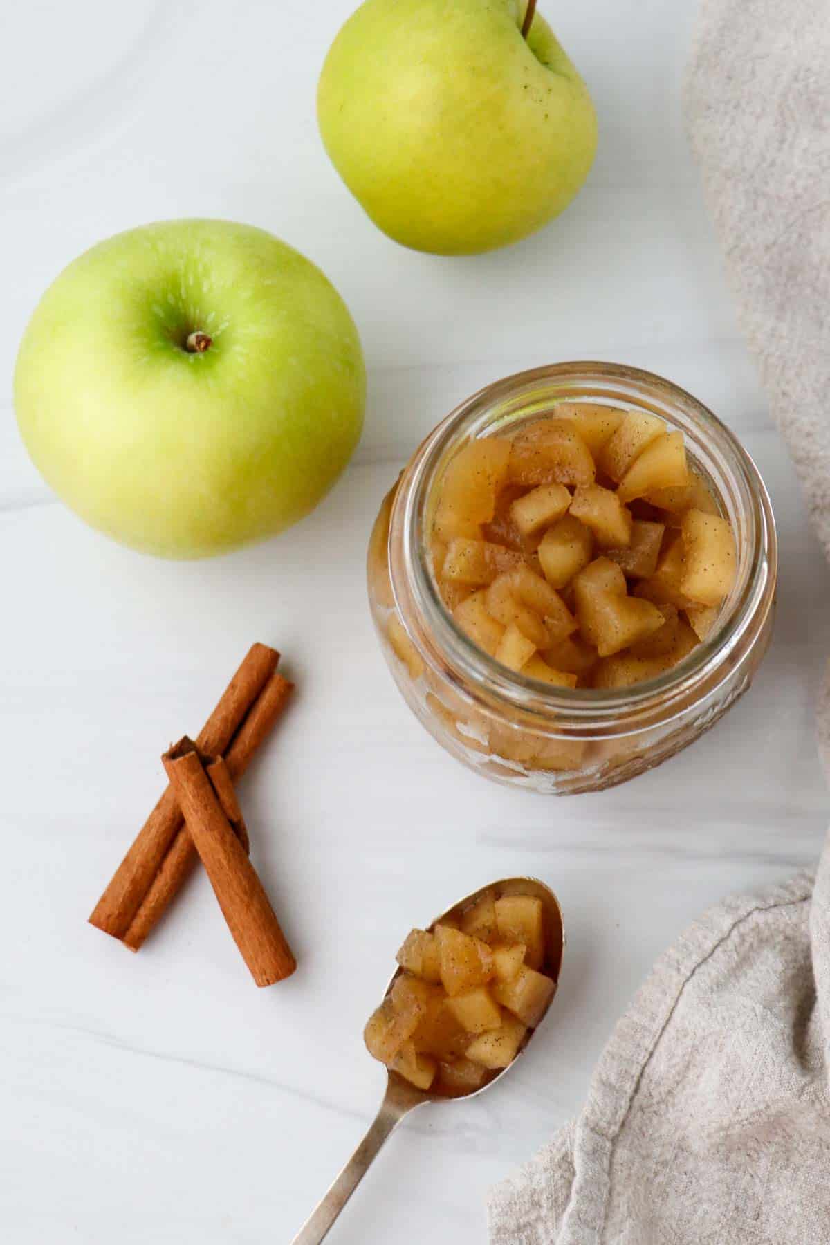 Overhead shot of apple compote with cinnamon sticks and apples.