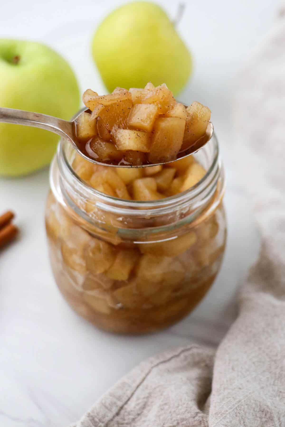 Spoonful of apple compote in front of a jar of compote and apples.