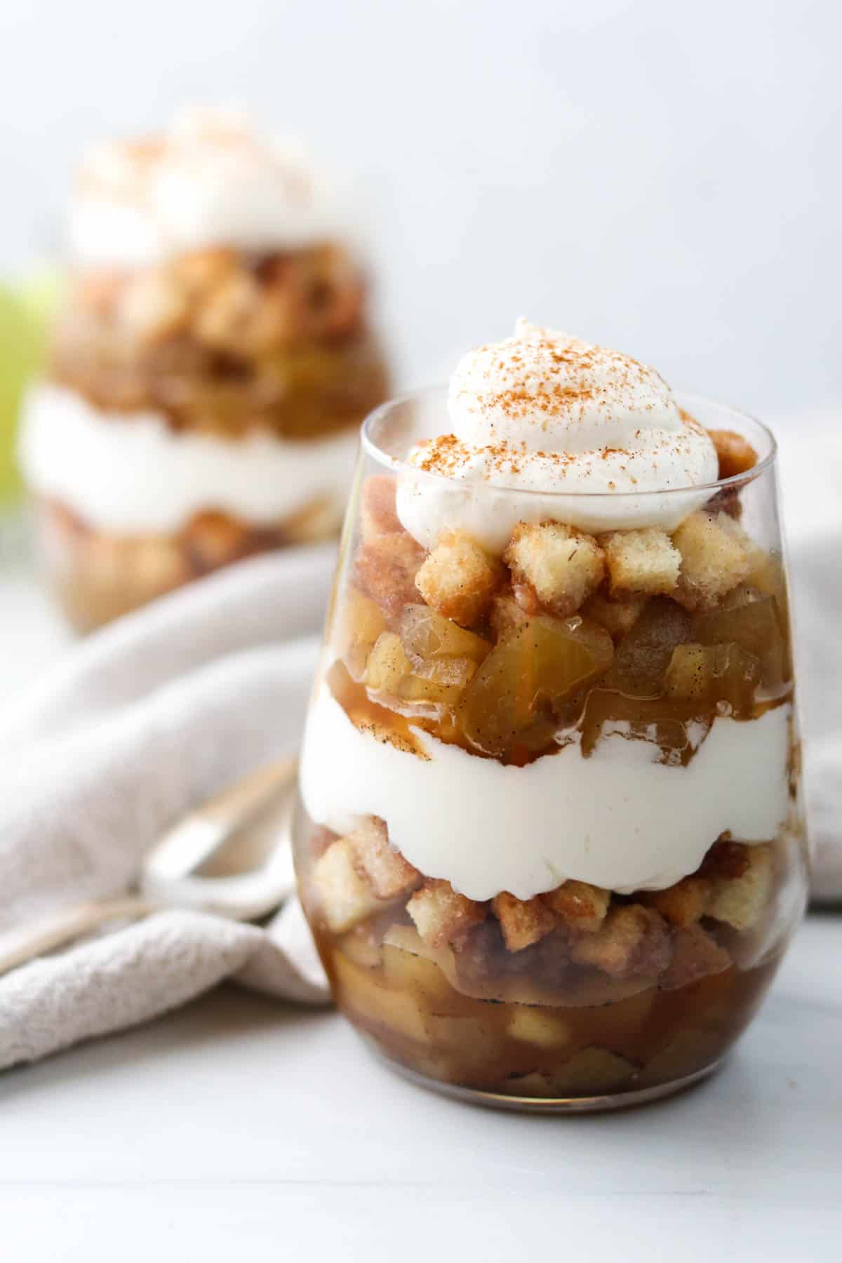 Apple trifle with whipped cream next to a napkin and spoon.