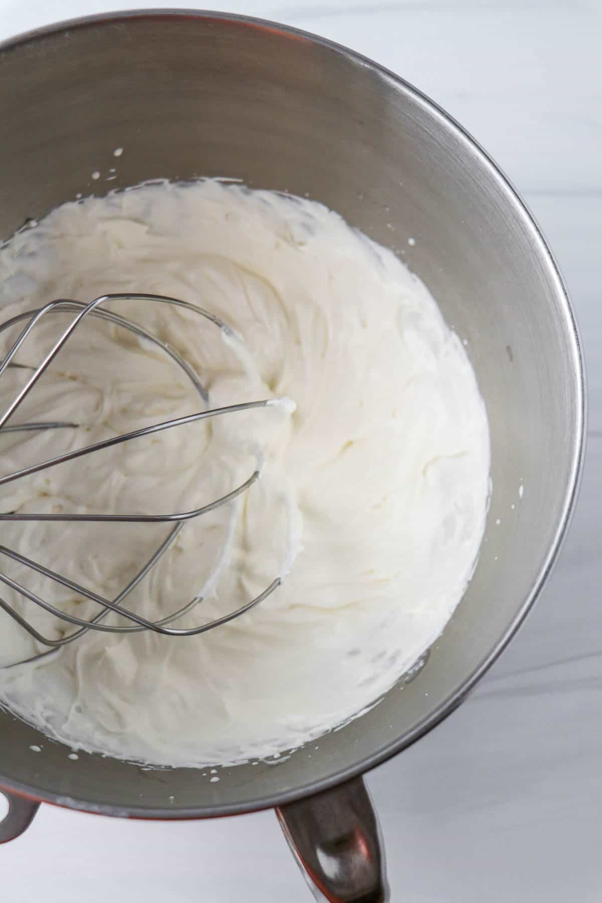 Whipped cream in a metal bowl with a whisk attachment.