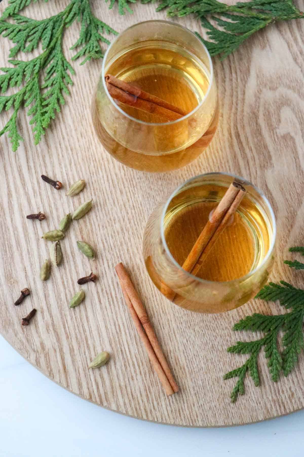 Two glasses of white mulled wine next to evergreen boughs and spices.