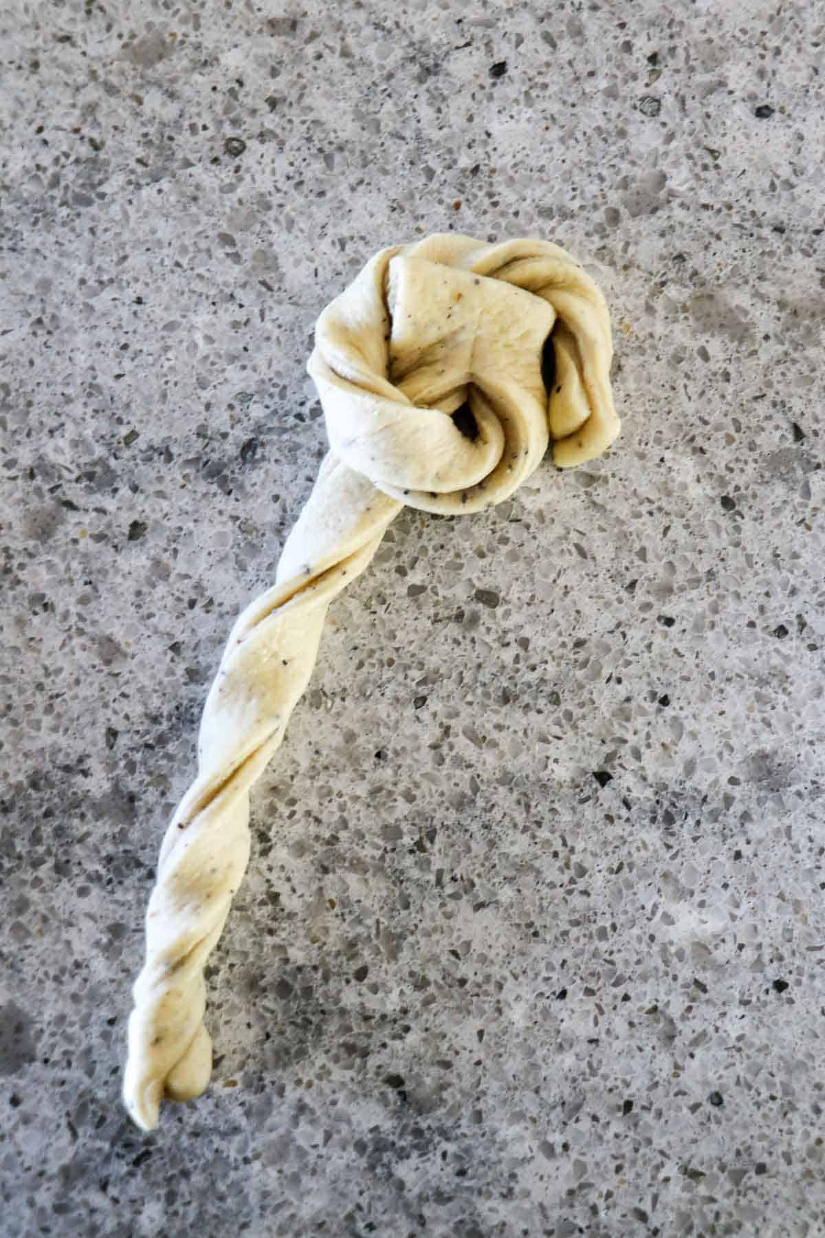 Cardamom bun in the process of being shaped on a gray counter.