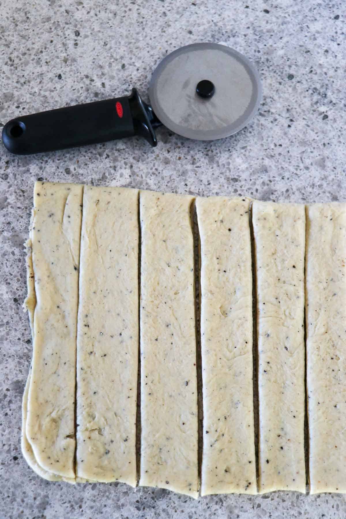 Strips of cardamom dough next to a pizza wheel.
