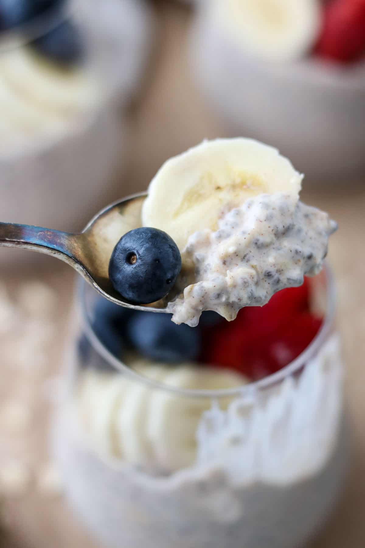 A spoonful of overnight oats, a banana slice and a blueberry on a spoon.