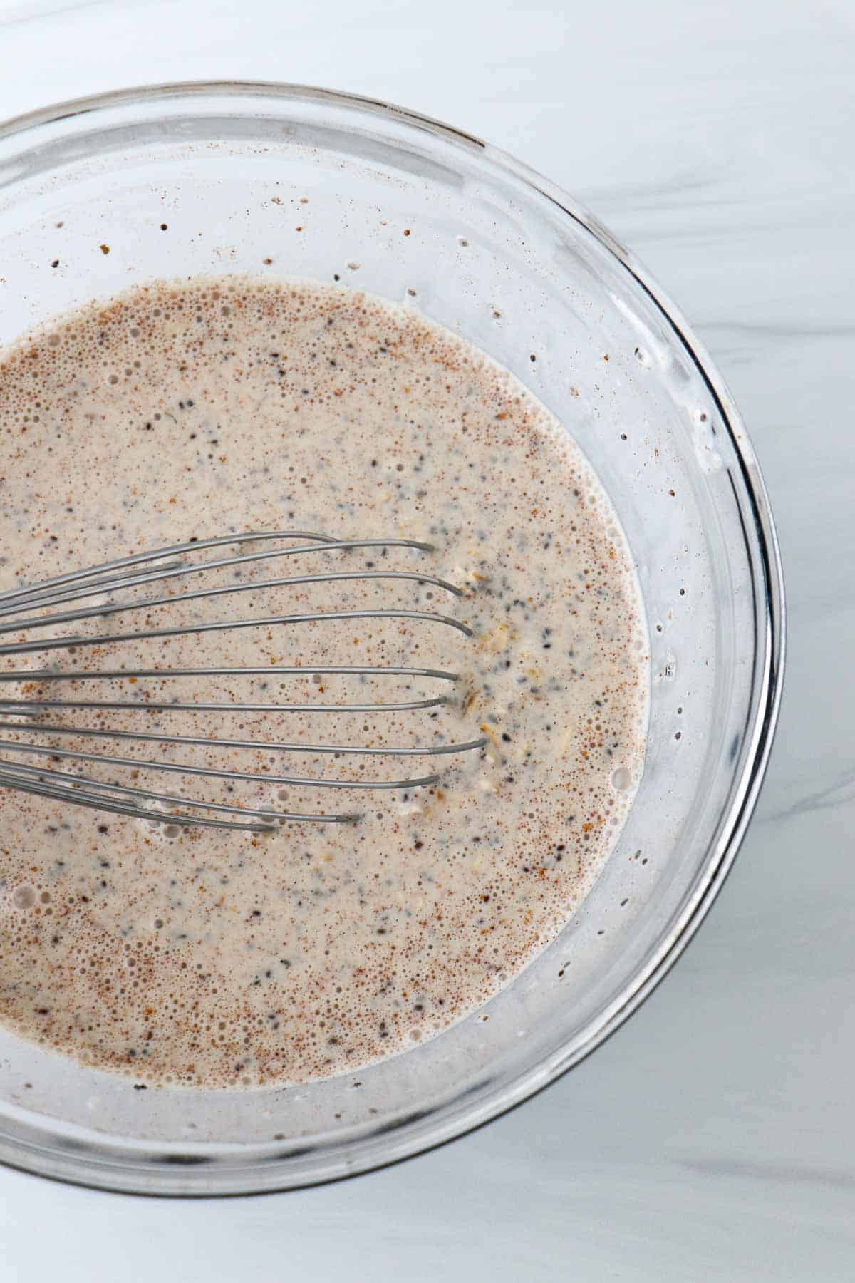 Overnight oats in a glass bowl with a a whisk.