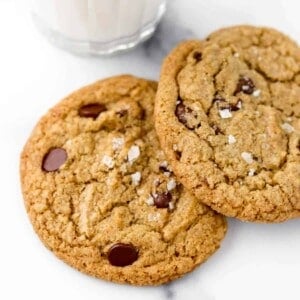 Close up of Rye Chocolate Chip Cookies sprinkled with sea salt next to a glass of milk.