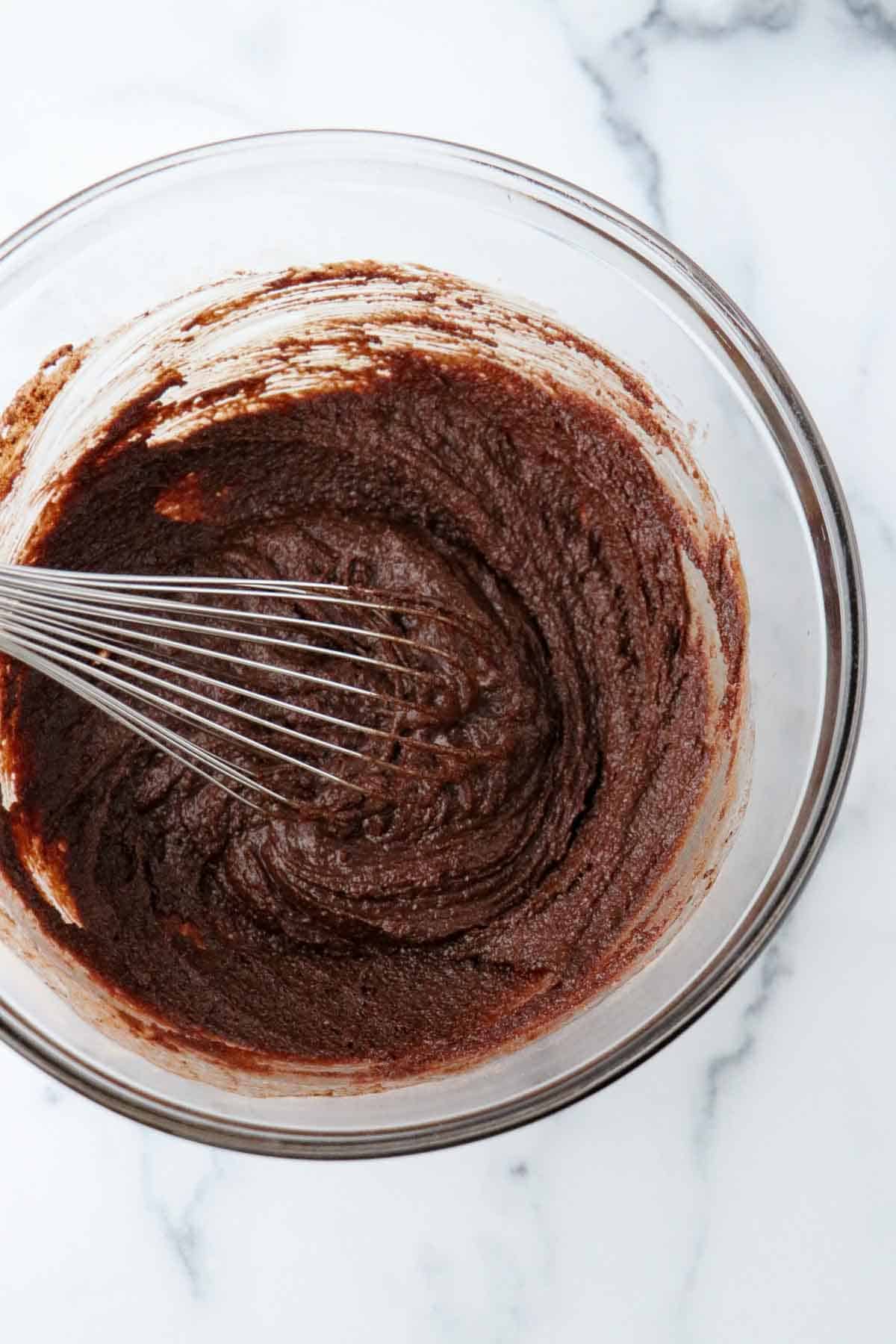 Chocolate cake batter in a glass bowl with a whisk.