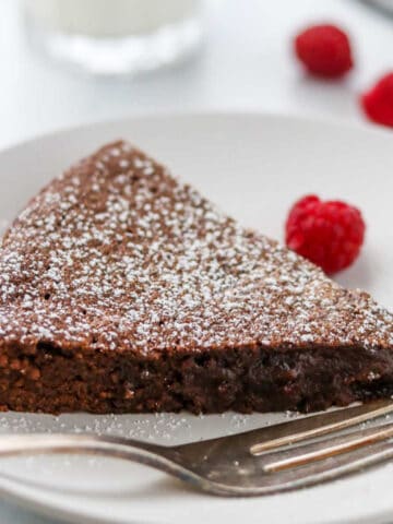 Closeup of a slice of kladdkaka on a plate next to a fork and raspberries.