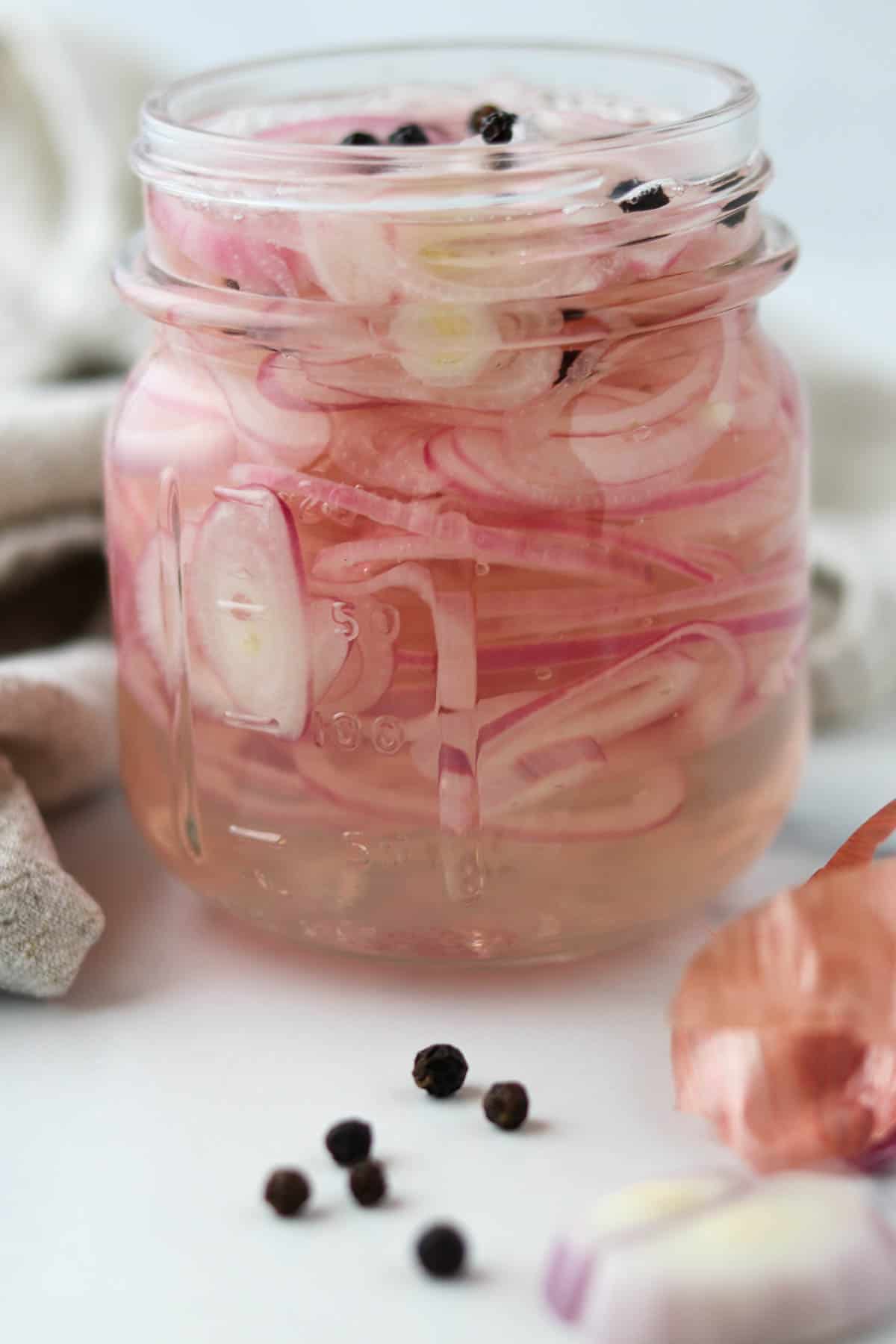 Quick Pickled Shallots in a jar with peppercorns.