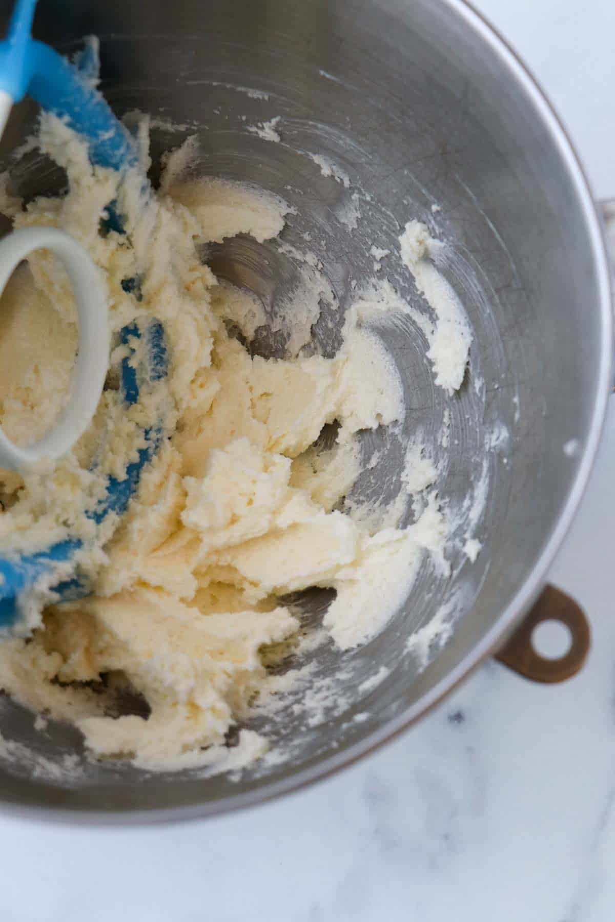 Butter and sugar creamed together in a metal bowl with a blue paddle attachment for a mixer.