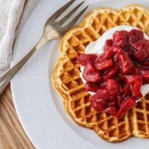 Waffle topped with Whipped Cream and Roasted Strawberries next to a fork.
