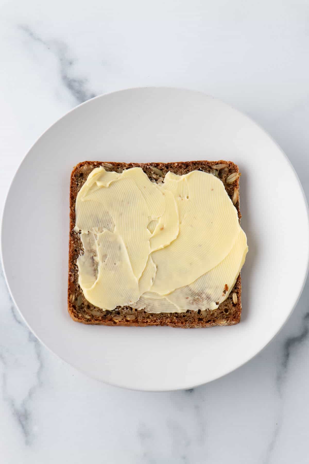 Buttered piece of rye bread on a white plate.
