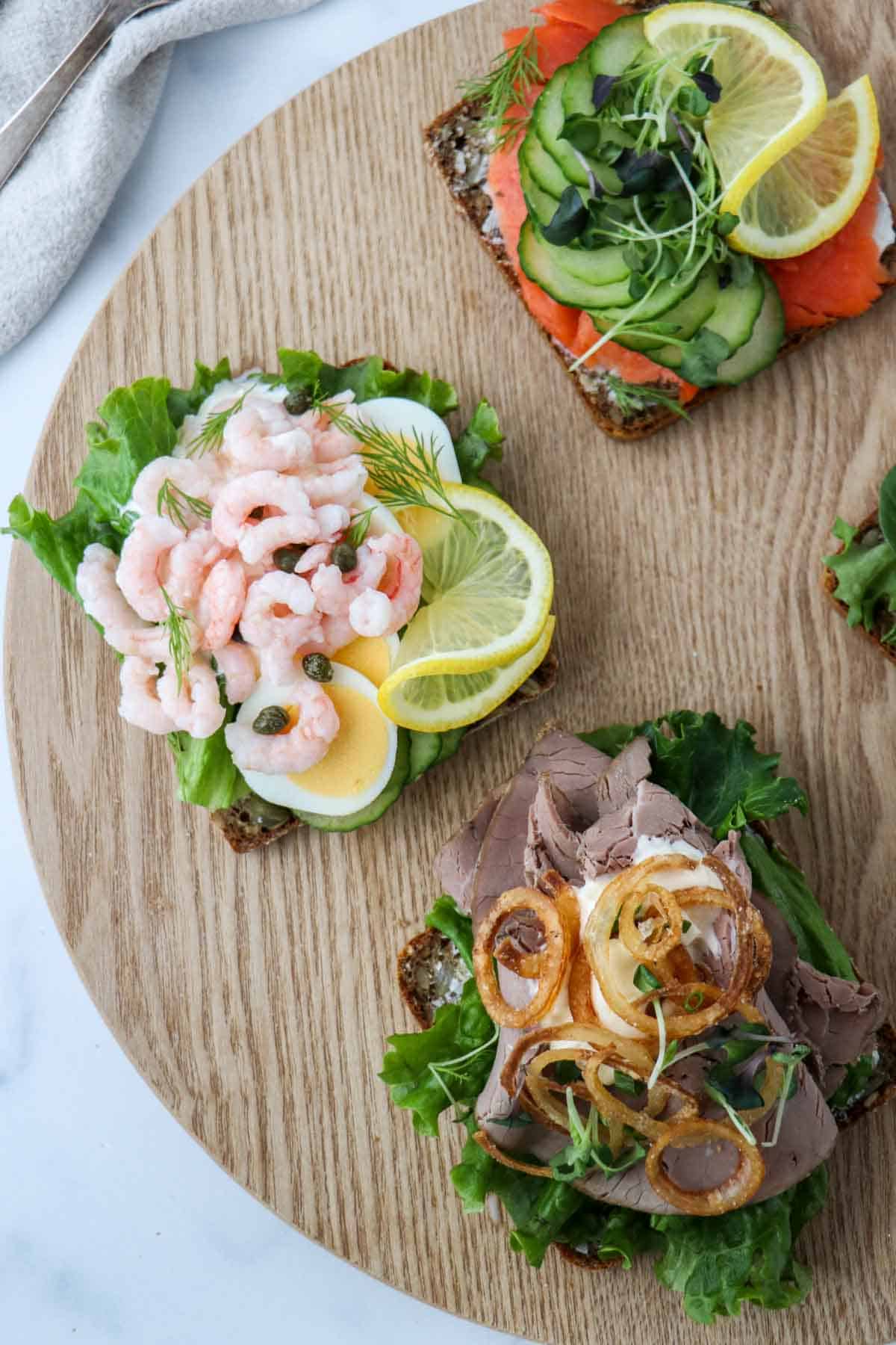 Three smørrebrød on a wooden platter.