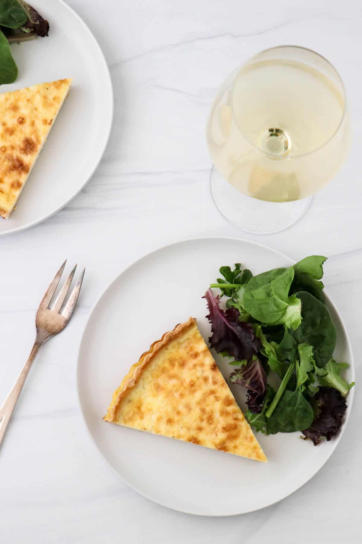 Swedish Cheese Pie (Västerbottenpaj) on a plate with salad next to a glass of wine and fork.