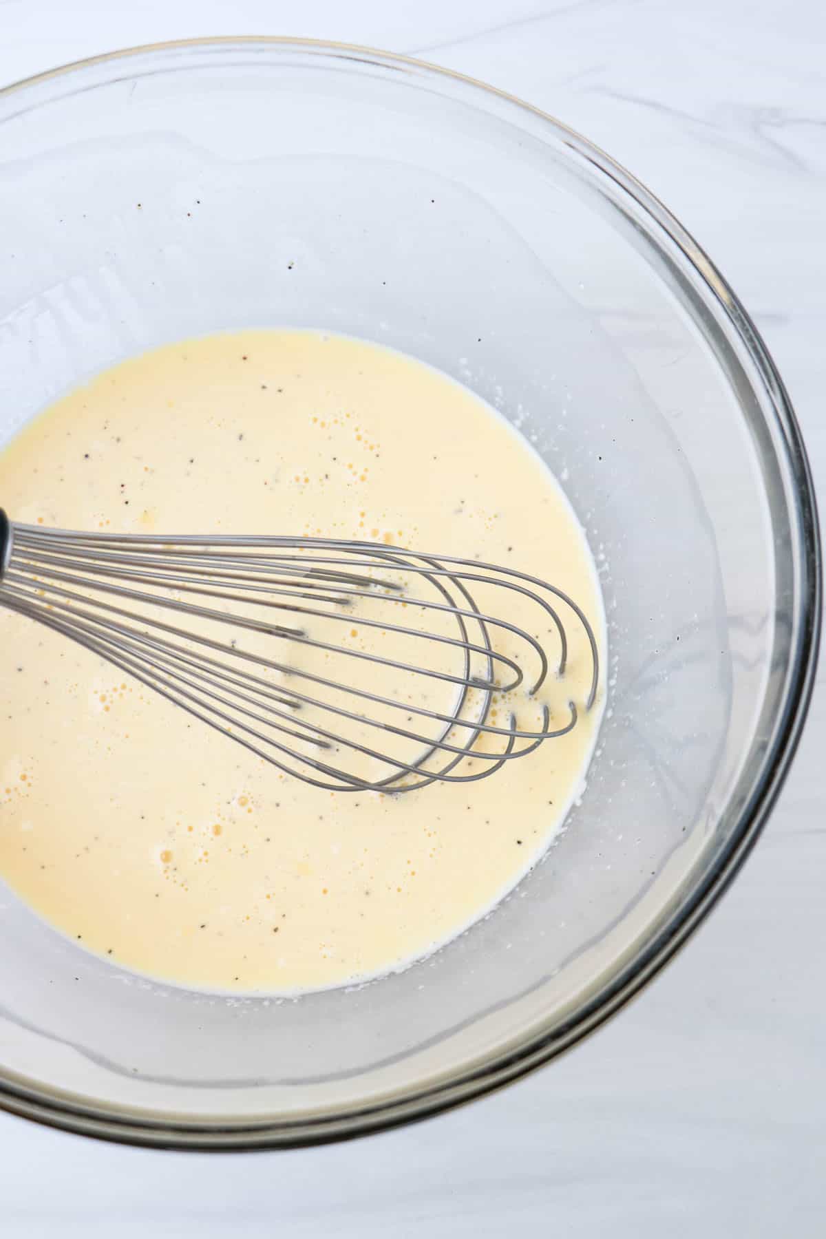 Eggs and milk whisked together in a glass bowl with a whisk.