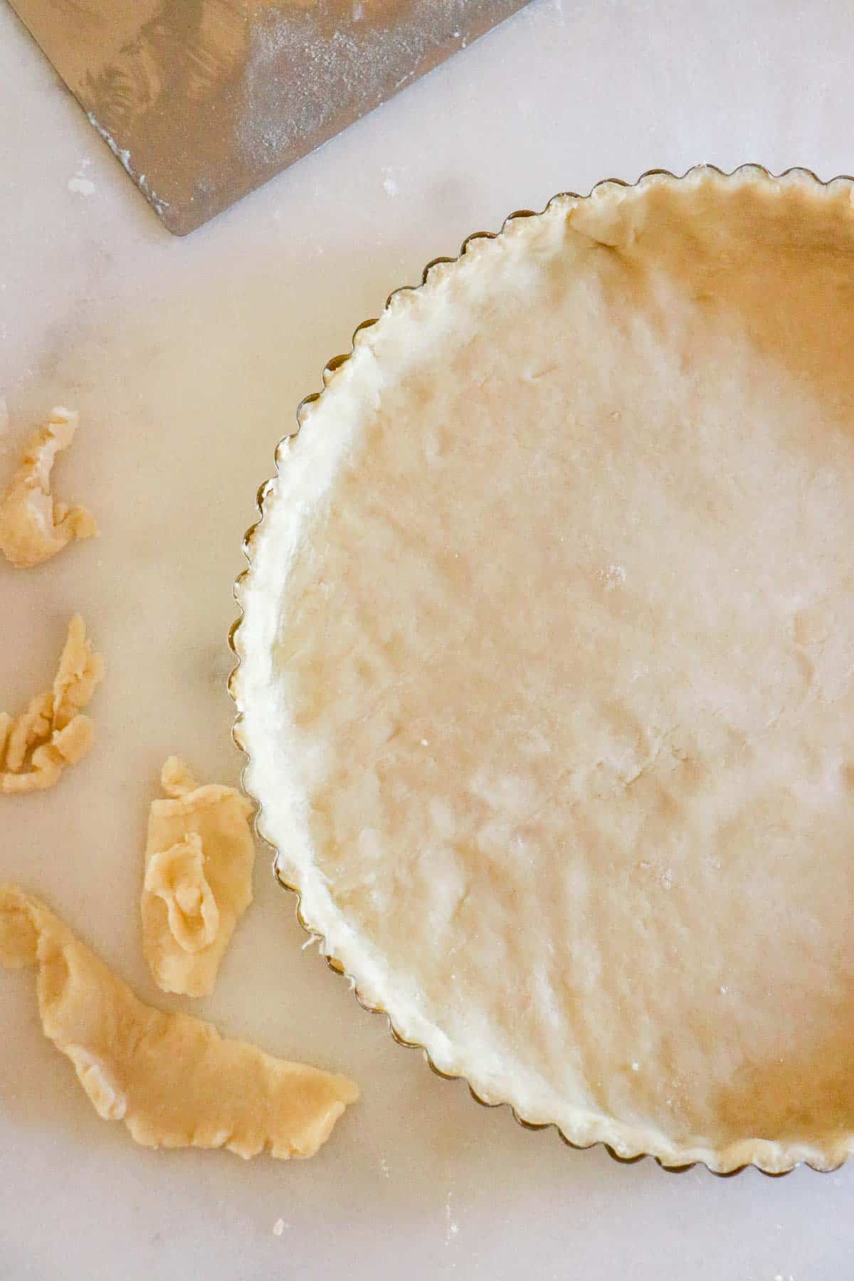 Unbaked pie dough in a tart pan next to scraps of dough.