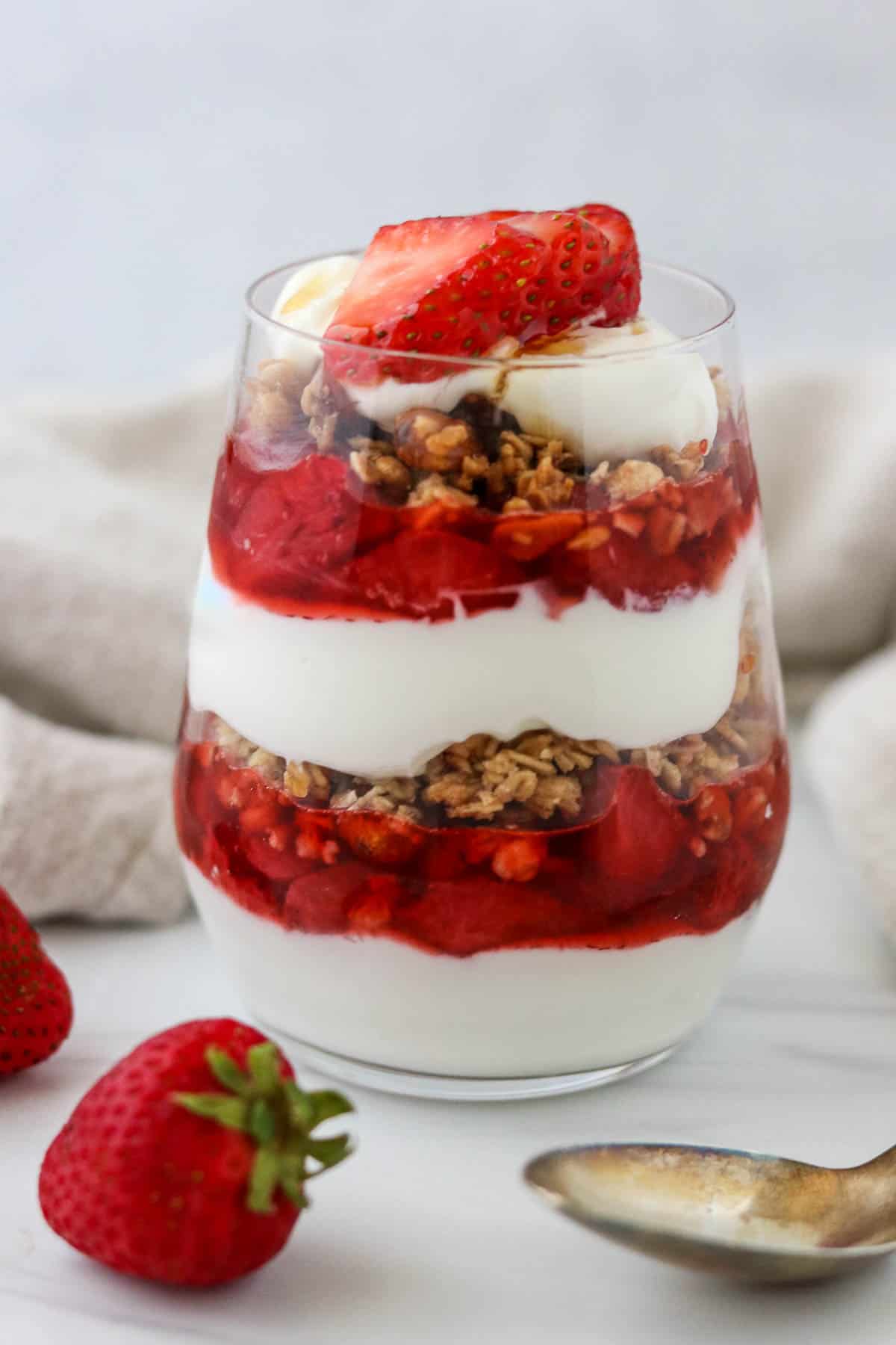 Strawberry granola and yogurt parfait next to a spoon and fresh strawberries.
