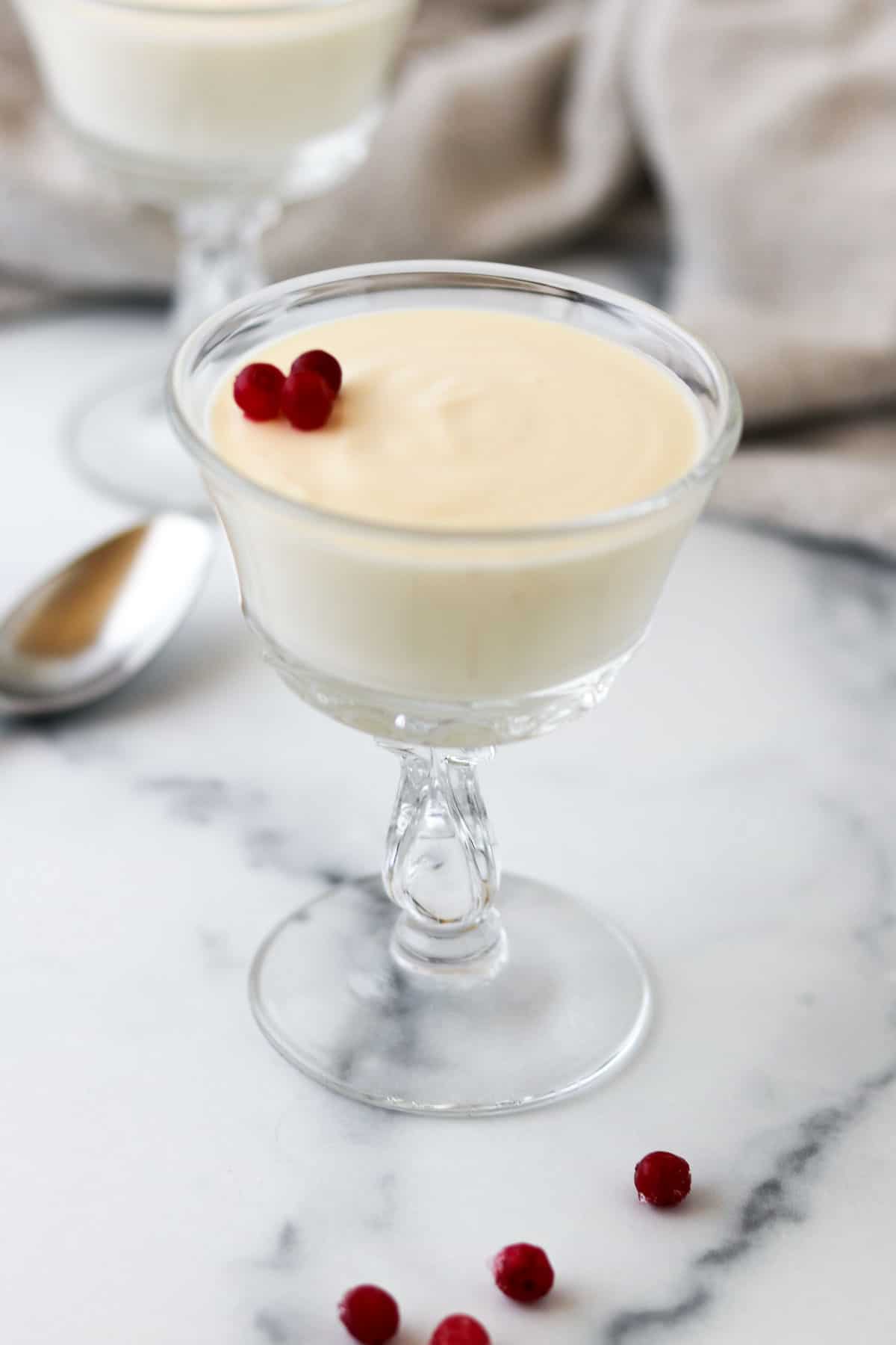Swedish Cream in a stemmed glass topped with lingonberries and next to a spoon.
