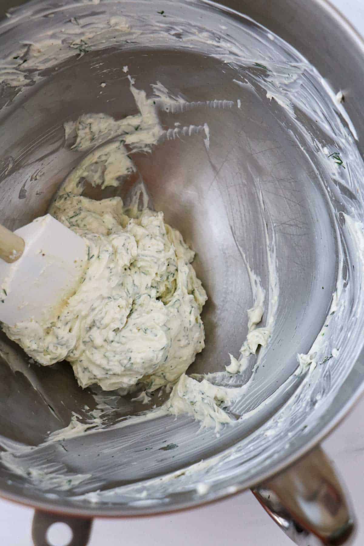 Cream cheese and dill mixture in a metal bowl with a rubber spatula.
