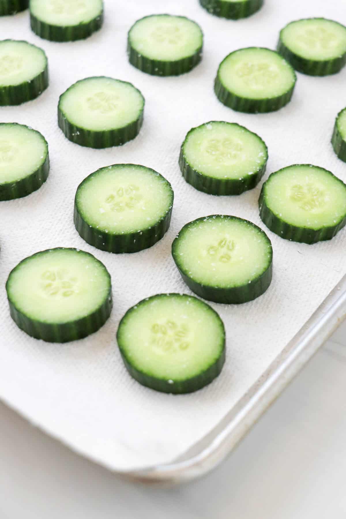 Salted cucumber rounds on a paper towel lined baking sheet.